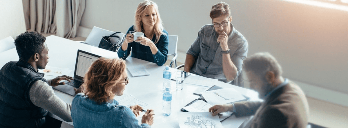 alt="people sitting around a desk at work"